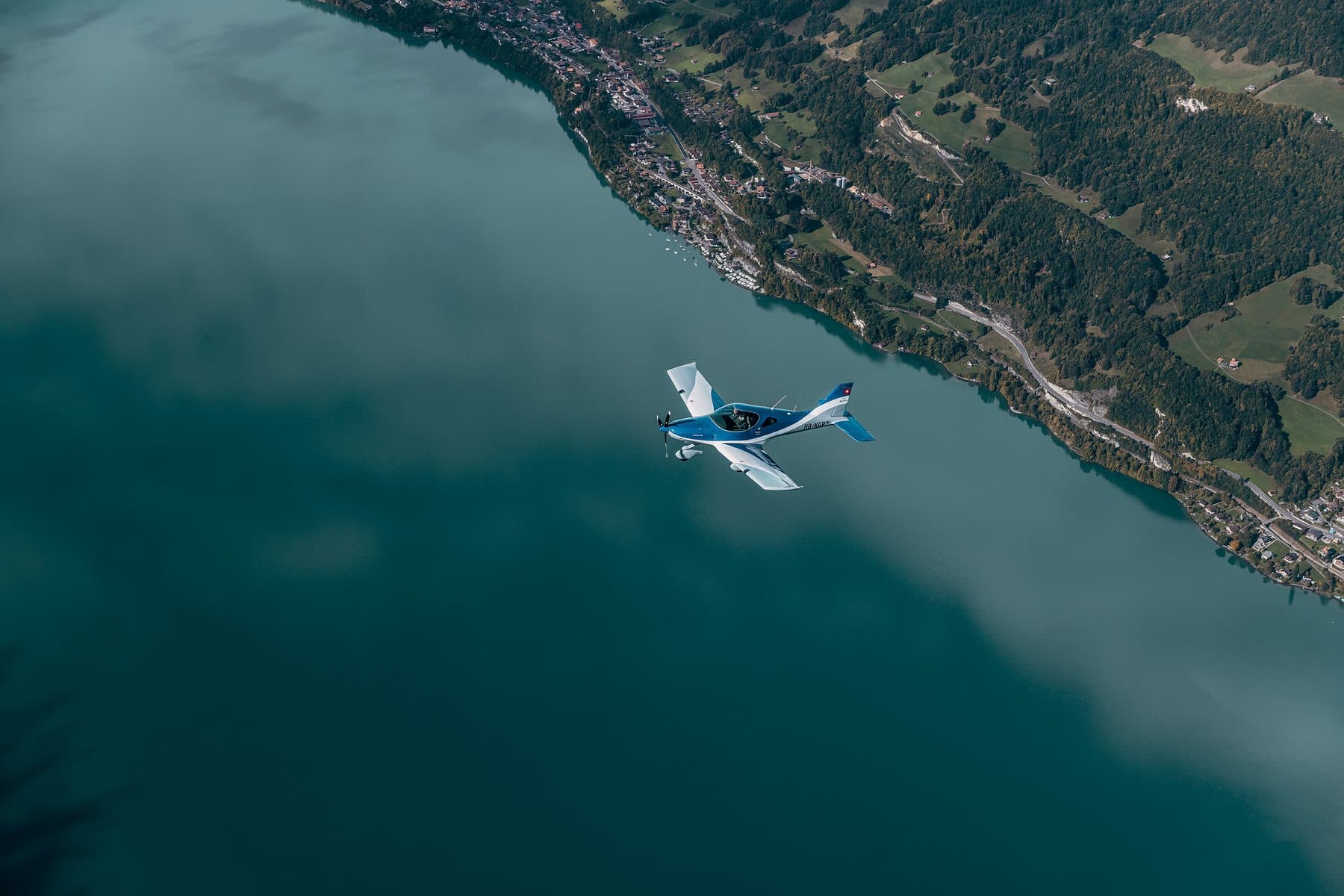 A light aircraft flying alone over a deep blue lake